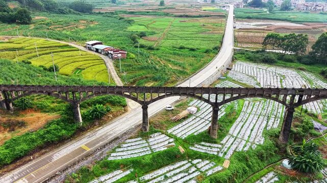 Cinematic aerial: Ancient stone aqueduct spanning karst mountains and green rice fields in Guangxi