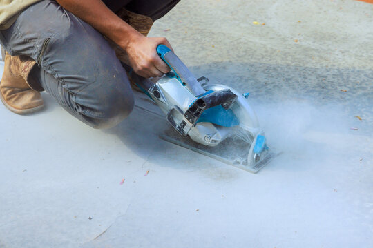 Worker cuts concrete with power saw while small dust clouds rise at construction site