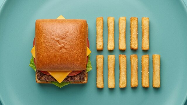 Square cheeseburger and organized french fries on teal plate in minimalist geometric studio flat lay
