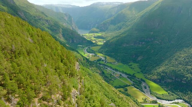 Aerial drone footage of Aurlandsdalen valley and the Aurlandselvi River in Aurland, Norway, showing a dramatic green mountain landscape, steep slopes, farmland and the winding river valley.