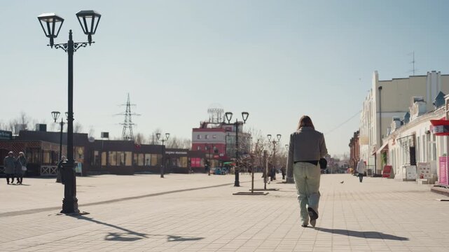 Pretty caucasian woman walking into distance, wide plaza framed by lamppost and pastel shops, long shadows, calm pace, contemplative traveler energy, minimal pedestrians and open horizon