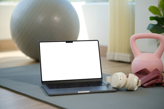 Laptop with a blank screen displayed beside home workout equipment for an online fitness session.