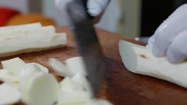 Side angle shot of peeled white Chinese yam being sliced into pieces.