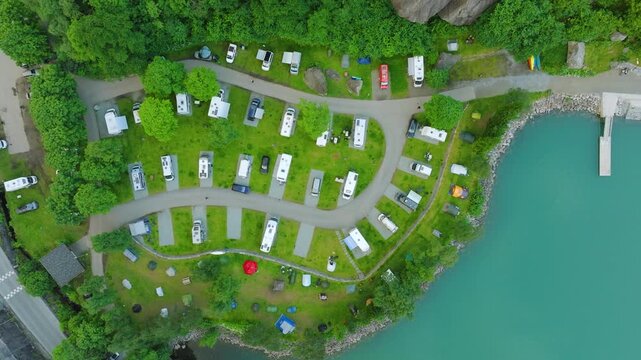 Aerial drone footage descending vertically over Trolltunga Camping beside Sandvinsvatnet in Odda, Norway. The campsite is surrounded by lush green mountains and the turquoise waters of the lake.