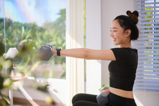 Young Asian woman performing a seated dumbbell exercise on a stability ball at home.