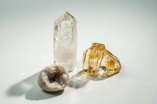 A collection of natural crystals including a tall clear quartz point, two golden citrine stones, and a small round geode on a white background