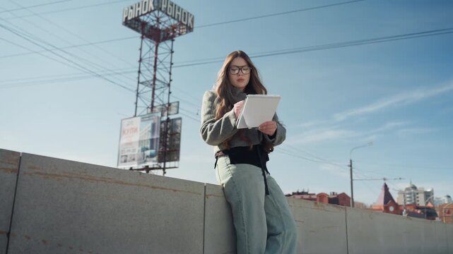 Selfassured lady vocalizing near busy streets. Female stands tall and speaks loudly by bustling city sidewalk. Graceful woman with assured posture reads aloud amidst vibrant street activity