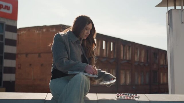 Pretty white woman sitting on rooftop playing small keyboard, thoughtful songwriter with grey coat and long brunette hair, brick factory backdrop, soft late light, intimate reflective atmosphere,