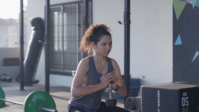 South Asian female athlete doing dumbbell goblet squats at an open-air rooftop gym. Medium close-up side angle shot with subtle camera tracking movement. Collection: WORKOUTSERIES2026.