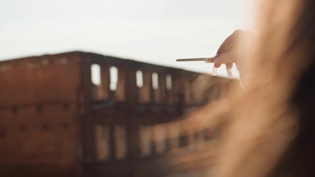 Hand offers fading sparkler toward weathered building, gentle flare and soft hair silhouette with painted nails, sunset glow and cinematic farewell mood