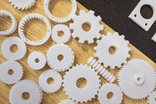 White plastic gears and cogs scattered on a wooden surface with a dark background, mechanical parts and design