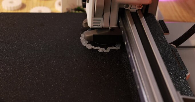 3d printer nozzle printing a small object on a black build plate in a home workshop, modern technology and manufacturing in progress.