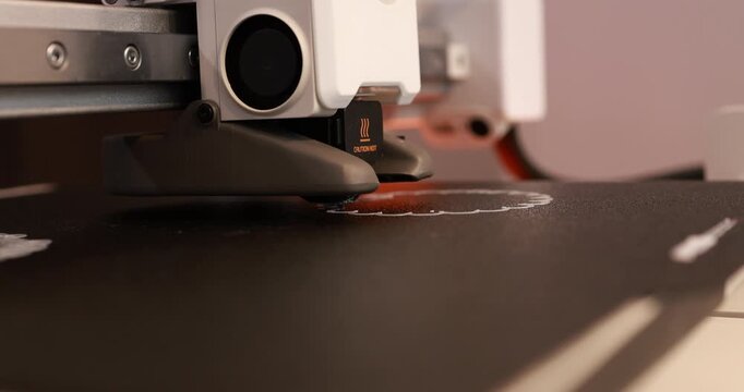 Close-up of a 3d printer nozzle printing red plastic on a build plate in a workshop, modern manufacturing and technology