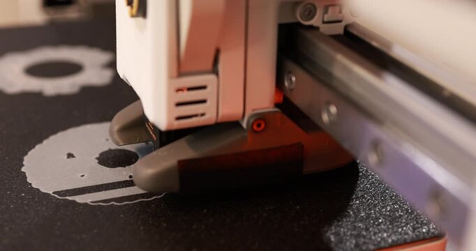 Close-up of a 3d printer head printing a white object on a black build plate with warm lighting and shallow focus