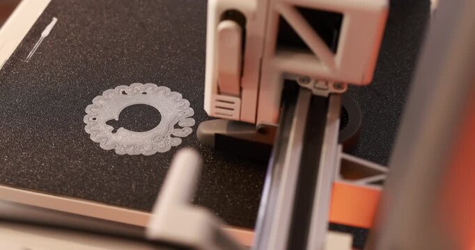 Close-up of a 3d printer printing a small decorative gear-like part on a build plate.