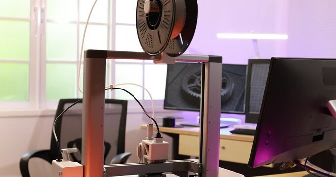 Close-up of a 3d printer head printing on a build plate in a modern workshop, with soft colored lights and shallow focus