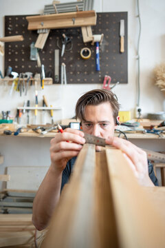 Man woodworker precisely measuring wooden board patch replacement for antique window frame, professional crafter holding ruler tool and checking exact size of details, preparing parts for repair.