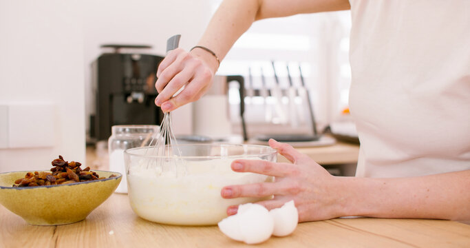Cooking food. Whisking process. Female chef hand mixing white wet ingredients mass for homemade dough in glass bowl on wooden table.