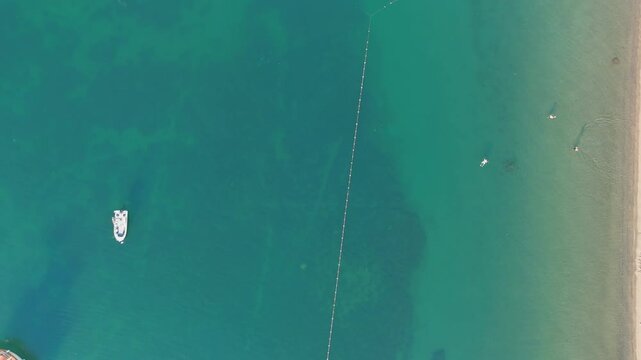 Marmaris, Turkey. Aerial top-down view of a wooden pier extending into turquoise Mediterranean water, with a traditional gulet moored alongside and leisure boats anchored nearby in morning calm. Aeri