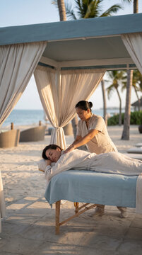 Woman receiving back massage inside a white curtained beach cabana