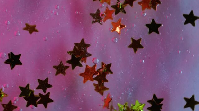 Astrology decoration. Wet texture. Green golden multicolor shiny stars water liquid sparkle gleam on abstract pink background.