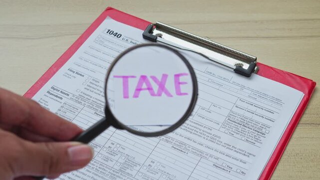 Hand uses magnifying glass to view taxes sticky note over 1040 tax form clipboard