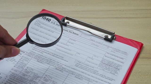 Hand uses magnifying glass to inspect 1040 individual income tax return form
