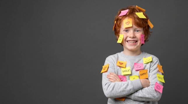 Smiling redhead boy with arms crossed covered in cheerful sticky notes