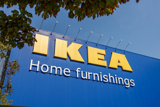 The yellow IKEA logo and Home furnishings wordmark on the blue store wall, with dark maple leaves arching into the frame from above.