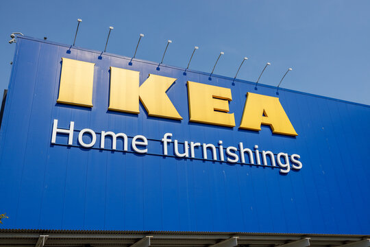 A tight low-angle shot of the bold yellow IKEA logo and Home furnishings wordmark against a bright blue wall, topped by a row of spotlights.