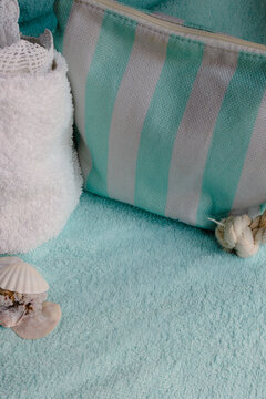 Striped beach bag and folded white towel resting on a soft blue green towel, accompanied by seashells, depicting a serene atmosphere for beauty and relaxation.Copy space. Branding design