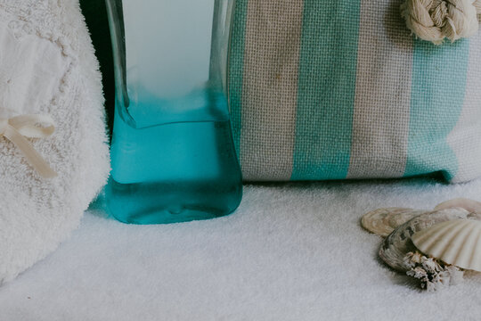 Pastel-toned background with spa essentials, soft white towels, a striped toiletry bag and decorative seashells, creating a serene atmosphere for well-being and self-care.