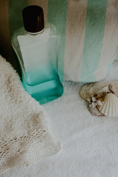 Spa bottle with aqua colored liquid, a soft white towel, and decorative seashells laying on a fluffy white surface, presenting a scene of calm, beauty, and peaceful self care