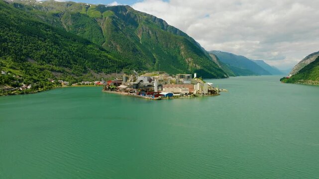 Aerial drone footage of Boliden Odda, a major zinc smelter located on the shore of S&oslash;rfjorden near Odda, Norway. The industrial complex stands against a dramatic landscape of steep green mountains 