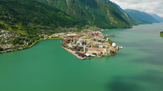 Aerial drone footage of Boliden Odda, a major zinc smelter located on the shore of S&oslash;rfjorden near Odda, Norway. The industrial complex stands against a dramatic landscape of steep green mountains 