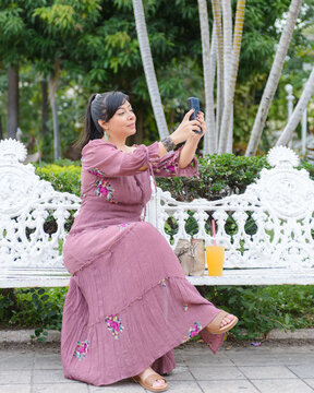 Cheerful Woman in Purple Dress Taking Selfie With Smartphone in Green Park