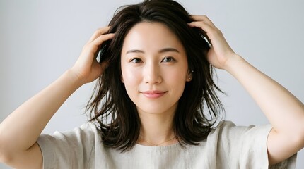 Fototapeta premium Casual portrait of a woman adjusting her hair against a soft neutral background.