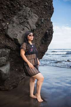 Smiling Woman in Black Lace Outfit Standing in Ocean Waves by Volcanic Cliff