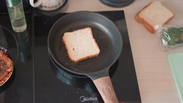 Slice of bread in pan on electric stove, unbuttered nonstick skillet, nearby wrapped herbs and cutting board, soft morning light, stillness and anticipation like fortune reading before toasting,