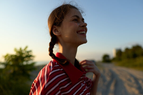 Happy woman lifestyle portrait outdoor at sunset. Young female person with pigtails smiling in summer warmth. Natural golden hour lighting, relaxed atmosphere, joyful mood, freedom concept.