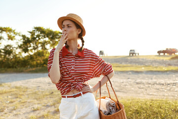 Obraz premium Young woman, lifestyle, straw, hat, cigarette, standing, outdoors. She wears striped shirt and white pants while posing in nature. Sunset lighting concept for leisure portrait.