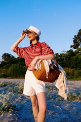 Obraz premium Young woman lifestyle traveler looking through binoculars on a summer day at the beach. She wears a vintage outfit with a basket. Concept of summer vacations, outdoor explorations, and travel.