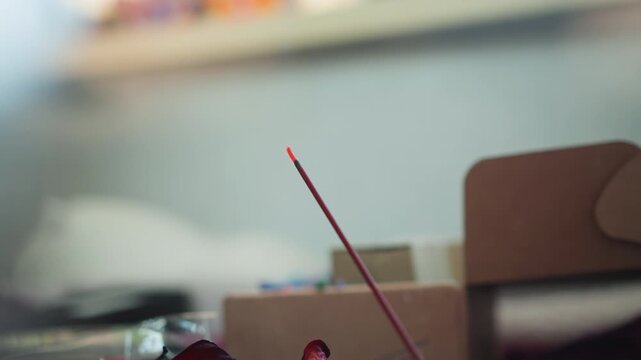 Single incense stick resting on box, hand reaches then withdraws leaving faint smoke trail, soft muted background and shallow depth, apprentice pauses in meditative aftermath, atmosphere