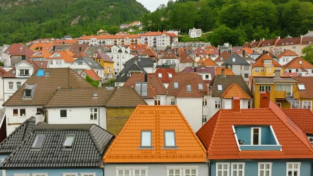 Smooth drone flight approaching a charming neighborhood of historic wooden houses in Bergen, Norway, revealing colorful facades, traditional tiled roofs and dense residential architecture against a lu