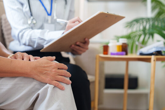 Close up of senior patient hands resting while doctor takes notes on clipboard during consultation
