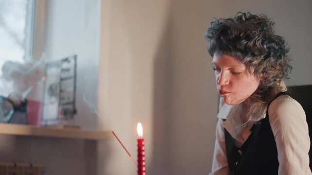 Caucasian fortune teller studies candle smoke with intense concentration in dim room, breath shaping patterns, delicate gestures, searching for omen and sign, atmospheric filmic lighting