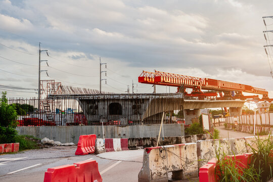 Image shows a construction site for a new concrete road and bridge, with large red steel beams and cranes at work a crucial infrastructure project for a major city.