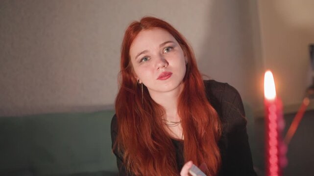 Closeup redhead seer by candle, young oracle leans forward breathing toward flame, lips pursed and eyes searching, warm candlelight highlights freckled skin, soft indoor background, introspective