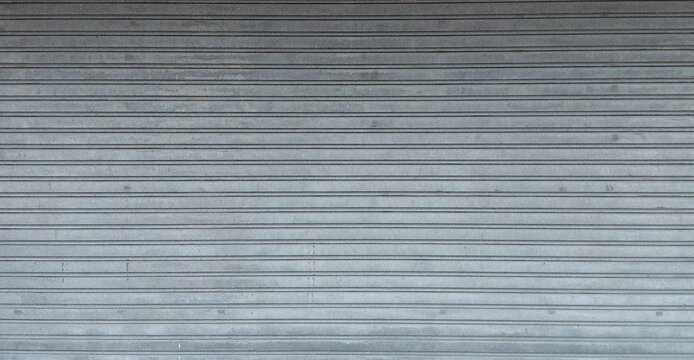 Full frame view of a grey metallic roller shutter door background texture with horizontal ribbed corrugated lines, industrial design concept.