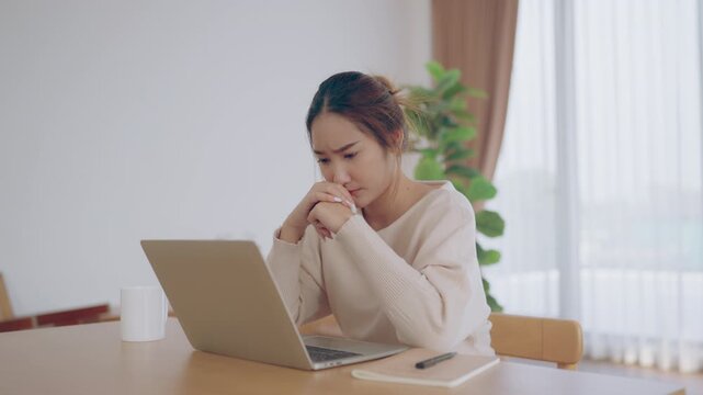 Young Asian woman working in living room, she has a headache due to long and overworking leaving her tired and dizzy. Concept of sickness from work and office syndrome